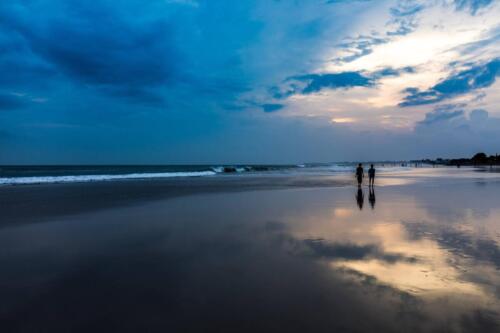 a couple walking in a beach with reflective sand